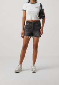 Biały krótki t-shirt z zielonym wykończeniem i logo. Czarniejece, przetarte krótkie spodenki jeansowe oraz szare sneakersy z fakturowanymi akcentami. Czarna torebka.