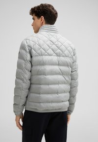 Giacca puffer grigia chiara con un motivo a rombi, colletto alto e polsini elastici, caratterizzata da una texture liscia e un design slanciato.
