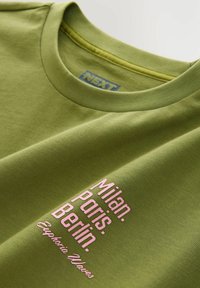 Zöld crew neck testpóló, rózsaszín felirattal, amelyen a Milano, Párizs, Berlin és az "Euphoria Waves" felirat található az elején.