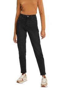 Zwarte jeans met een hoge taille en een strakke pasvorm, voorzien van achterzakken en een subtiele gestructureerde stof, gecombineerd met beige en bruine sneakers.