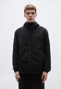 Must kerge jope lukuga, reguleeritava kapuutsi ja elastsete mansettidega. Omab lihtsat disaini ja esiküljel paneelide detaile.