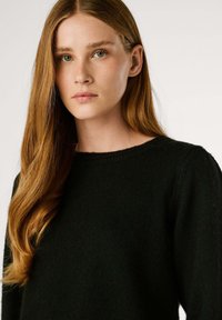 Melna adīta džemperis ar apaļu kakla izgriezumu, ar mīkstu tekstūru un ribotu apakšmalu. Garas piedurknes papildina brīvo piegriezumu.