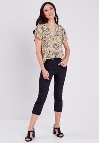 Bloomprint top in geel, zwart en oranje, V-hals, korte mouwen; gecombineerd met zwarte cropped broeken en peep-toe blokhakken.