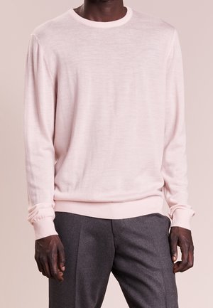Hellrosa Pullover mit Rundhalsausschnitt aus weichem Stoff, mit langen Ärmeln und gerippten Bündchen, kombiniert mit dunkelgrauen Hosen.