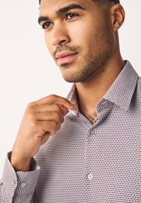 Chemise pour homme à boutons avec un petit motif à carreaux bordeaux et blanc, dotée d'un col intérieur contrastant et de boutons gris.