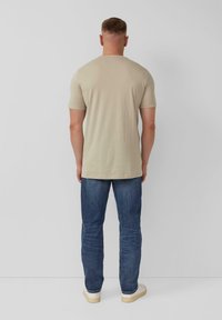 Beige t-shirt met korte mouwen, slim-fit ontwerp, gladde textuur, gedragen met donkerblauwe jeans en witte schoenen, gezien vanaf de achterkant.