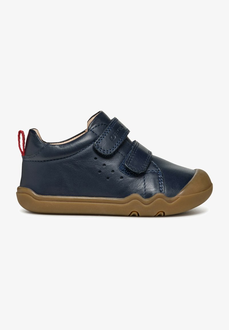 Scarpe in pelle blu marine con due cinturini in velcro, suola in gomma beige, punta arrotondata e perforazioni decorative ai lati. Dettaglio sul tallone rosso.