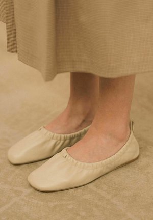 Bailarinas de cuero beige con puntera redonda, cuello elástico y textura suave, sobre una superficie de color claro.