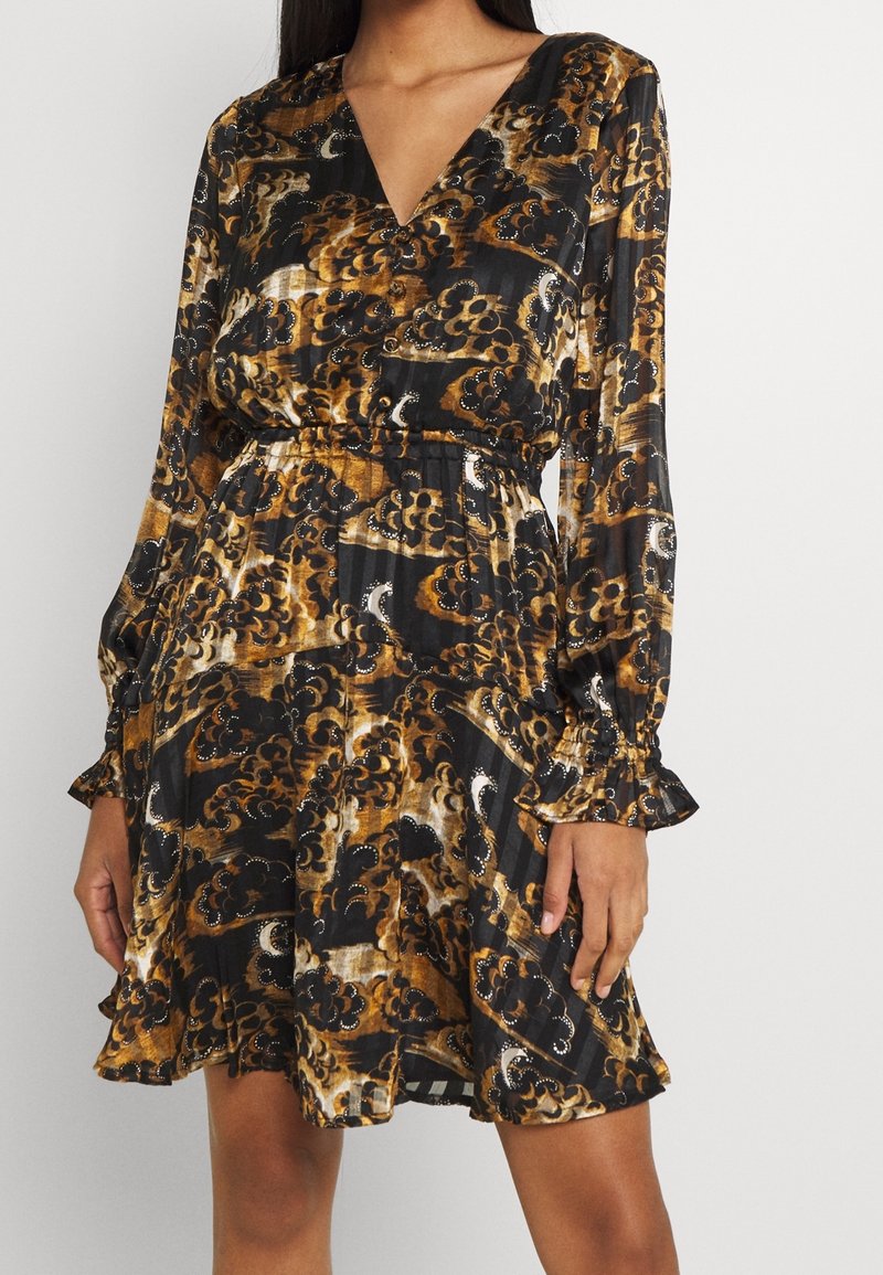 Vestido negro y dorado con estampado, que presenta mangas largas, escote en V, y un lazo en la cintura, con dobladillo con volantes y detalles de tela texturizada.