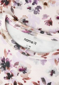Chemise pour enfants à motif floral avec des fleurs roses, violettes et marron, affichant l'étiquette de la marque "name it" et la taille EU 92 US 2T à l'intérieur du col.