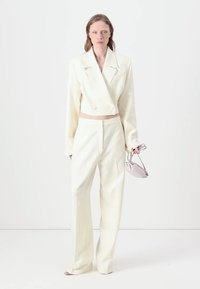 Cropped double-breasted blazer and high-waisted trousers in textured off-white fabric, paired with a small lavender handbag.