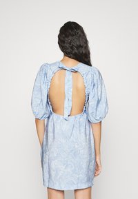 Ljusblå klänning med puffärmar, en ryggöppning med knytning och ett marmor mönster på ett mjukt strukturerat tyg.