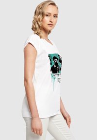 Weißes Baumwoll-T-Shirt mit lockerem Schnitt, V-Ausschnitt, das mit einem grafischen Druck in Schwarz und Türkis sowie Text und Spritzern gestaltet ist.