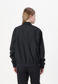 Black bomber jacket with a relaxed fit, elastic cuffs and hem, and a smooth, matte finish. Back view shows a simple, minimalist design.