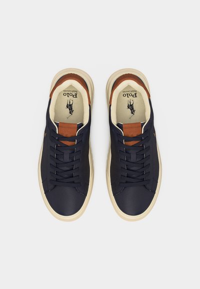 Paire de baskets basses bleu marine avec semelles blanches, patch en cuir marron sur la languette, et logo Polo Ralph Lauren imprimé à l'intérieur.