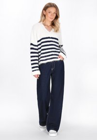 V-Ausschnitt, flauschiger weißer Pullover mit navyblauen horizontalen Streifen; kombiniert mit lässigen, dunkelblauen Jeans und weißen Sneakers.