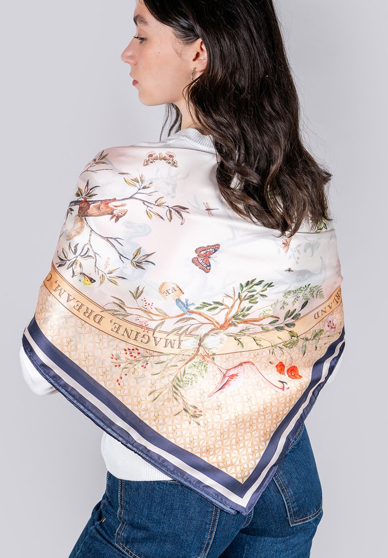 Seidenschal mit einem hellen Blumenmuster und Vögeln, umrandet von marineblauen und goldenen geometrischen Designs, über einer Schulter drapiert.