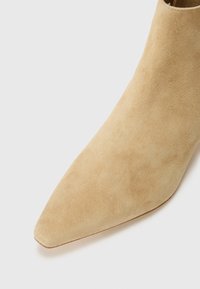 Beige suede ankle boot with a pointed toe, smooth texture, and streamlined design. Minimalist style with no visible hardware or accents.