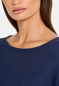 Marineblaues Strickoberteil mit weitem Halsausschnitt und strukturiertem Stoff, ausgestattet mit kurzen Ärmeln und einer lockeren Passform. Glatter, definiert sichtbarer Schlüsselbeinbereich.