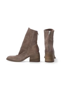 Bottes chelsea brunes en daim avec un design perforé. Elles possèdent une fermeture éclair sur le côté et un talon empilé en bois pour plus de stabilité.