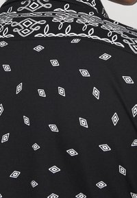 Svart skjorta med vita diamantsymmetrier och blommig broderi, med en strukturerad tyg och klassisk kragsdesign.