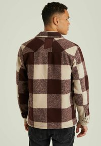 Rood en beige geruit flanelen jack met een spitse kraag, knoopmanchetten en een schouderdetail aan de achterkant. Zachte textuur en een ontspannen pasvorm.