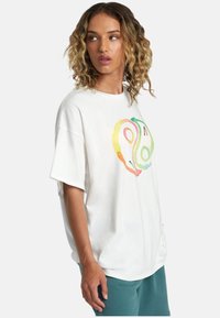 Camiseta de algodón blanca de gran tamaño con un gráfico abstracto y colorido de aguacates en la parte delantera. Mangas cortas y un corte relajado.