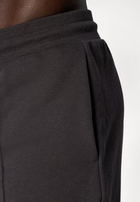 Sorte idrettsshorts laget av myk, teksturert stoff med elastisk midjebånd og sidelommer. Designet for komfort og bevegelse.