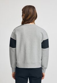 Felpa grigia con accenti neri a blocchi di colore sulle maniche, colletto e polsini a costine. Materiale morbido, vestibilità comoda e cuciture rinforzate.