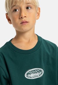 Camiseta de algodón verde con un logotipo gráfico blanco que presenta un globo y el texto "dc shoe company". Cuello redondo clásico y textura suave.