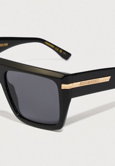 Gafas de sol rectangulares negras con lentes oscuros y acentos dorados del logo de DSQUARED2 en las patillas sobre un fondo blanco.