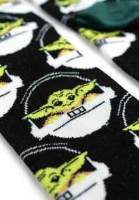 Calzini neri con un motivo ripetuto di un personaggio dei cartoni animati con la pelle verde, grandi orecchie e tratti del viso espressivi su uno sfondo bianco.