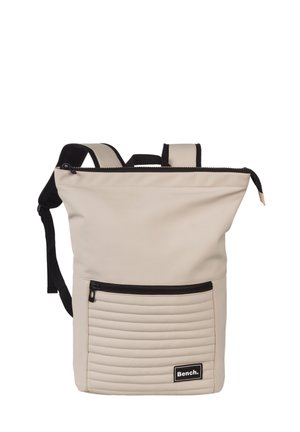 Beige rugzak met een ritssluiting aan de bovenkant, een getextureerd paneel aan de onderkant met verticale ribbels, verstelbare zwarte riemen en een voorvak met rits.