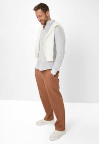 Striped button-up shirt in light blue and white, paired with rust-colored pants and white sneakers. Sweater draped over shoulders.