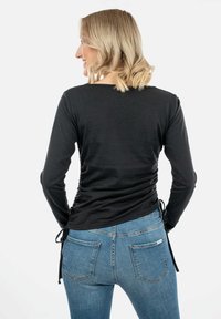 Must musta varrukatega topp, mille külgedel on voldid, reguleeritavad sidemed taljes, sobitatud siniste teksadega, millel on tagakotid.