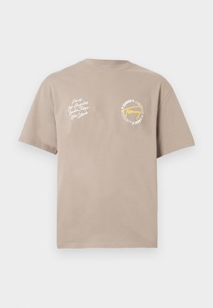 Bež kratka majica s bijelim rukopisnim imenima gradova na lijevoj strani prsnog koša i okruglim Tommy Jeans logotipom sa žutom podcrtavanjem na desnoj strani prsnog koša.