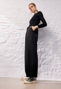 Top lungo aderente nero a maniche lunghe abbinato a pantaloni neri a vita alta e gamba larga, con tasche, e sneaker metallizzati con finitura testurizzata.