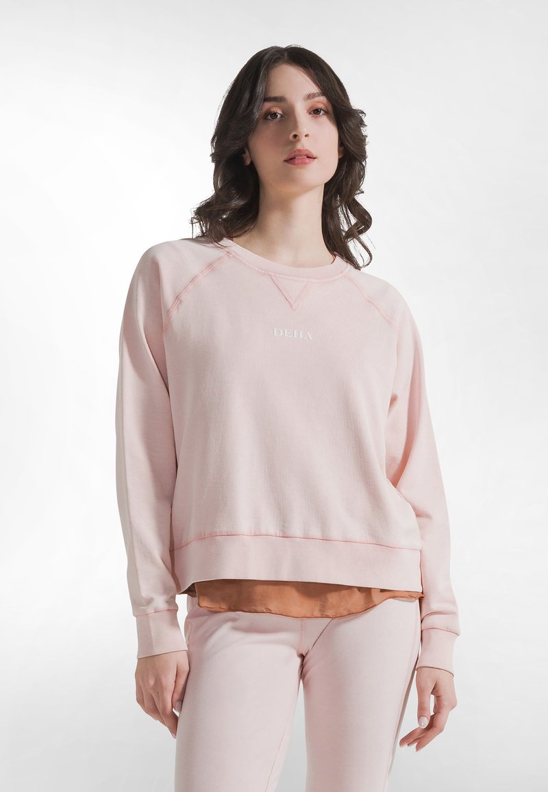 Sudadera rosa claro con cuello redondo, mangas largas y puños acanalados. Presenta una capa inferior en un tono más oscuro que contrasta.