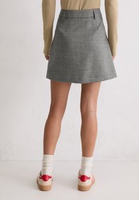 Szara spódnica w kratę o rozszerzanym kroju, charakteryzująca się gładką fakturą i subtelnym połyskiem. Noszona z beżową bluzką z długim rękawem i butami na platformie.