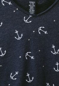 Marinblå t-shirt med vita ankar mönster och små silvriga stjärnor. Tillverkad i mjukt tyg med rundad halsringning och etikett inuti.