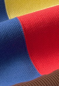 Gros plan d'un tissu tricoté avec des blocs de couleurs bleu, rouge, jaune et marron montrant la texture et les détails du tissage.