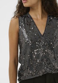 Flitterekkel díszített felső V-nyakkivágással, sötét anyagalappal és csillogó ezüst és fekete flitterekkel, amelyek texturált felületet hoznak létre.