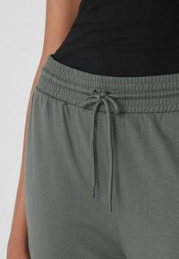 Primer plano de pantalones verde con cintura elástica y cordón atado, combinados con una camiseta negra acanalada.