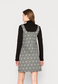 Vestido de gingham preto e branco com padrão floral, decote quadrado nas costas e bainha godê, usado sobre um suéter preto de gola alta.