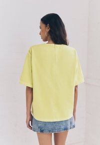 T-shirt gialla oversize con maniche corte, collo rotondo e dettaglio con cucitura centrale. Abbinata a una minigonna di jeans.