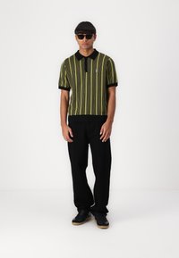 Black and yellow striped polo shirt with a collar and short sleeves, paired with black pants and black shoes, worn by a person.