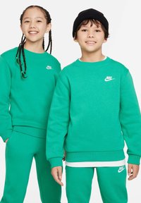 Zeleni Nike duksevi i trenirke s rebrastim manžetama i pojasom. Bijeli logo na lijevoj strani prsnog koša i lijevoj strani bokova. Crni kapica na jednom modelu.