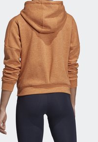 Sweat à capuche orange texturé avec capuche à cordon, manches amples et ourlet côtelé. Porté avec des leggings foncés.