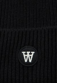 Close-up of black ribbed knit fabric with a circular black patch displaying a white stylized "AA" logo stitched in the center.