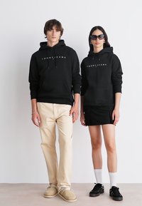 Sudaderas negras con el logo "TOMMY JEANS", combinadas con pantalones beige y una falda negra. Los accesorios incluyen gafas de sol y zapatillas.